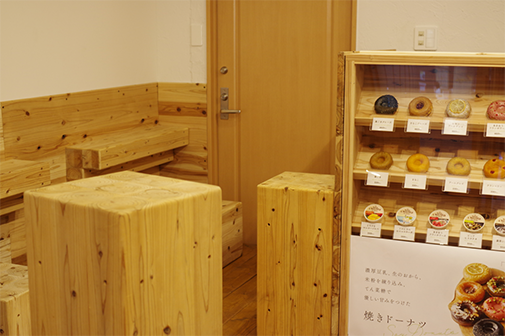 Soy storiesの店内。ベージュ色の木材と白い壁紙で、木でできた椅子や机が置かれている。端にはドーナツのショーケースが写っている。